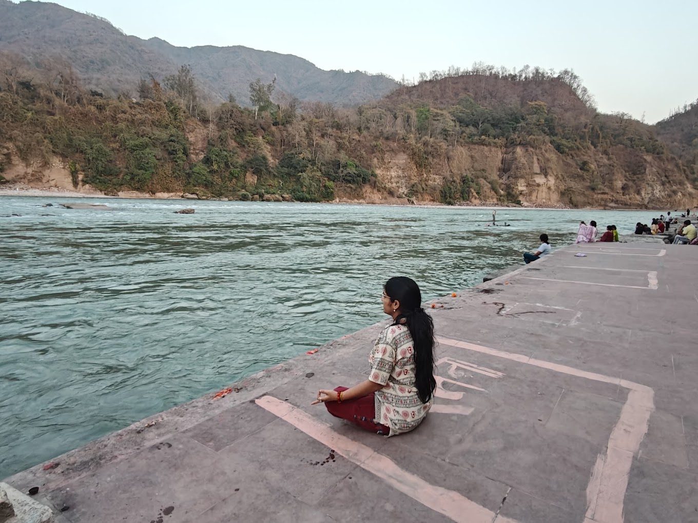 Dr. Kaushal seated in meditation on a riverbank ghat with hills behind